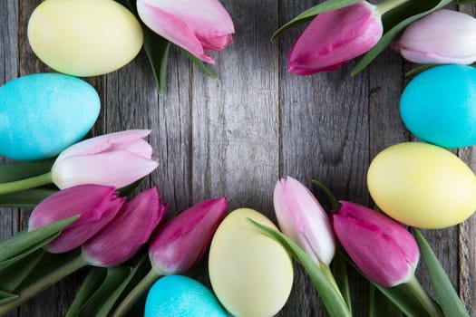 Tulips and colorful easter eggs in wooden background with copy space in center