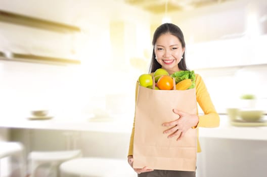 Young Asian woman hand holding shopping paper bag filled with fruits and vegetables in kitchen.