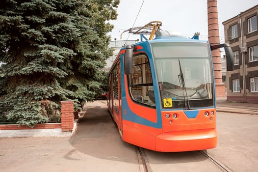 New red and blue tram is in a park, ready to travel the route. yellow sign invalid driving