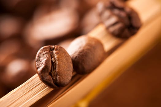 Close-up of individual coffee beans on the edge of a braided basket. The focus is on the foremost coffee bean.