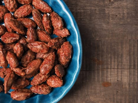 Tasty roasted almonds in a blue ceramic bowl with ingredients on wood