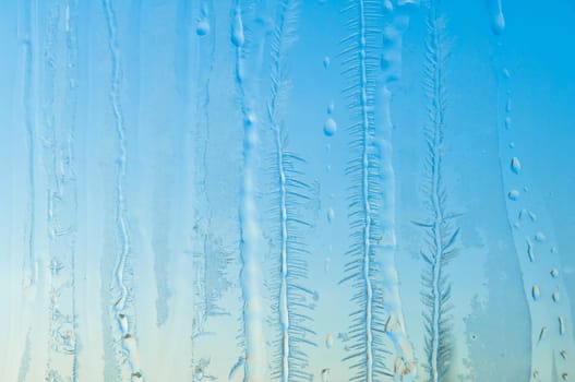 Melted and frosted ice pattern on frosty window glass in winter