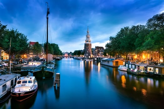 Beautiful night in Amsterdam. Night illumination of buildings and boats near the water in the canal.