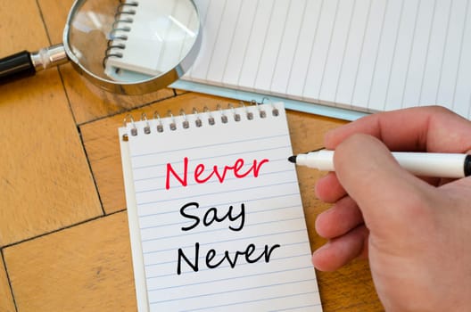 Human hand over wooden background and never say never text concept