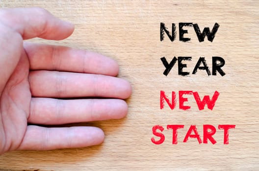 Human hand over wooden background and new year new start text concept