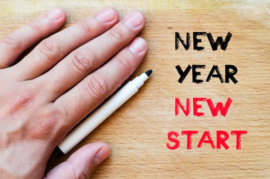 Human hand over wooden background and new year new start text concept