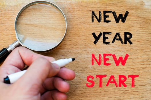 Human hand over wooden background and new year new start text concept