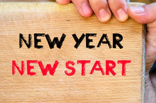 Human hand over wooden background and new year new start text concept