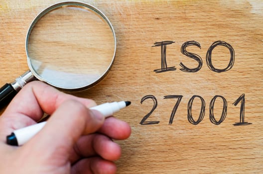 Human hand over wooden background and iso 27001 text concept