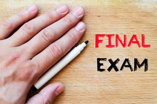 Human hand over wooden background and final exam text concept