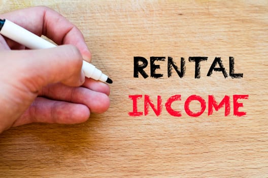 Human hand over wooden background and rental income text concept