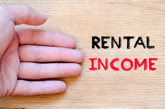 Human hand over wooden background and rental income text concept