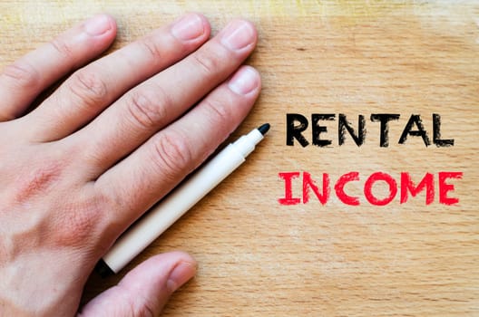 Human hand over wooden background and rental income text concept