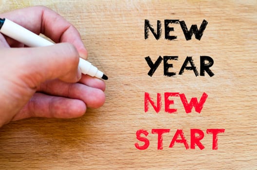 Human hand over wooden background and new year new start text concept