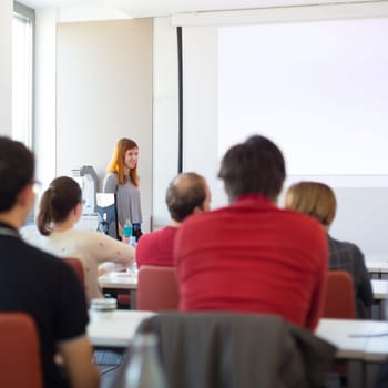 Speaker giving presentation in lecture hall at university. Participants listening to lecture and making notes.