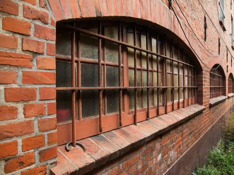 Perspective view along a brick wall with barred windows.