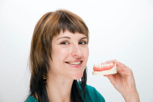 Head portrait of a young brunette woman against a white background holding an artificial dentition in front of her.