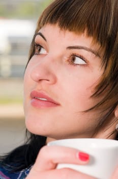 Close up a young woman with a white cup held in front of her mouth looking to the side.