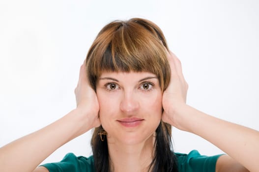 Head portrait of a young brunette woman against a white background holding her ears.