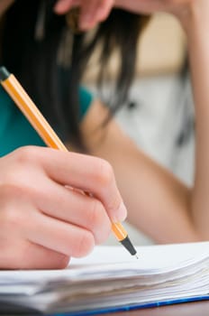 Wide-angle close-up of a young woman's right hand sitting at the home table with pen in hand.