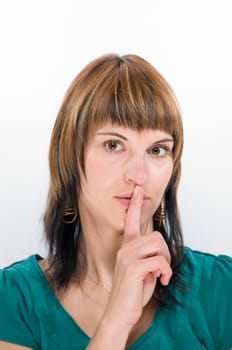Head portrait of a young brunette woman against a white background laying her finger on her mouth.