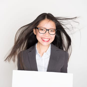 Portrait of Asian businesswoman in formalwear smiling and hand holding white blank paper card, standing on plain background.