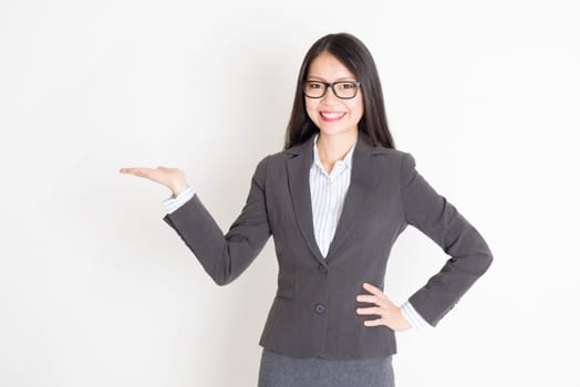 Portrait of Asian businesswoman in formalwear smiling and hand holding something, standing on plain background.
