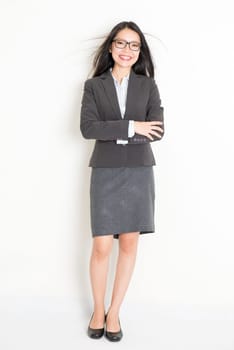 Portrait of young Asian business woman in formalwear smiling, full body standing on plain background.