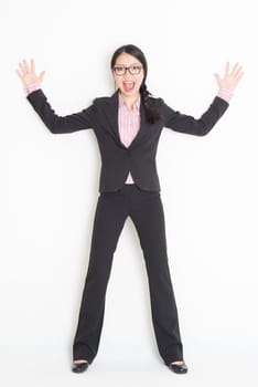 Full length front view of shocked young Asian businesswoman in formalwear leaning on wall, standing on plain background.