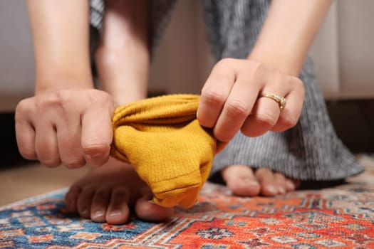 A person pulls off a yellow sock while sitting on a colorful rug.