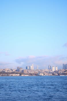 Modern structures rise above the waterfront near the tranquil blue sea.
