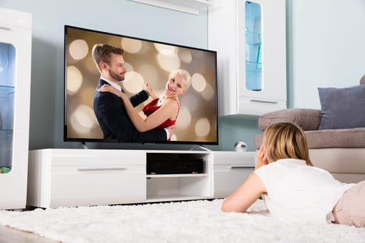 Young Woman Lying On Carpet Watching Romantic Movie On Television At Home