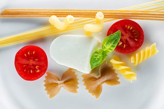 Dry pasta with mozzarella cheese and tomatoes on white background
