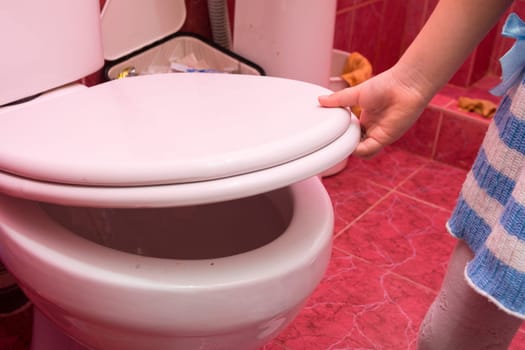 Child's hand down the toilet lid and seat, close-up