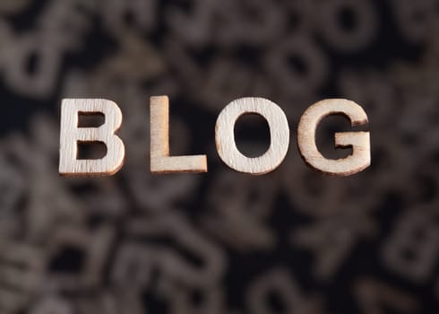Blog wooden letters text created in wood floating above random letters below out of focus on a black background
