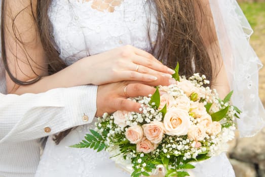 Hands of newlyweds with rings, against a wedding bouquet