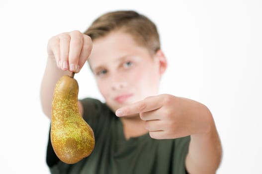 Frontal head and shoulder view of a young male teenager against a white background with his right hand holding a pear in front of him and pointing to the fruit with his left index finger