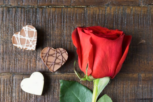 Bright red rose and three heart shaped chocolates