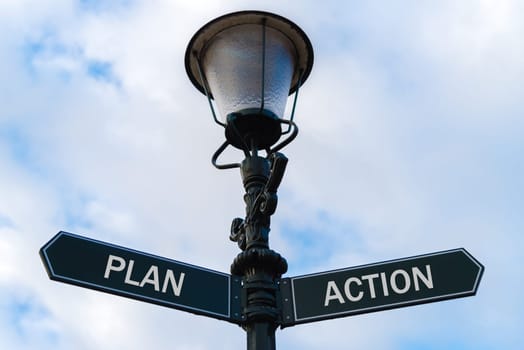 Street lighting pole with two opposite directional arrows over blue cloudy background. Plan versus Action concept.