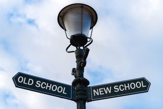 Street lighting pole with two opposite directional arrows over blue cloudy background. Old School versus New School concept.
