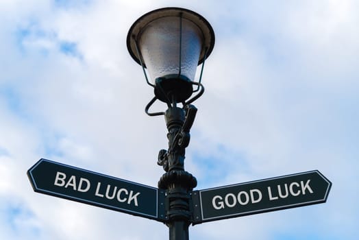 Street lighting pole with two opposite directional arrows over blue cloudy background. Bad Luck versus Good Luck concept.