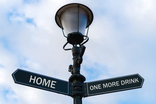 Street lighting pole with two opposite directional arrows over blue cloudy background. Home versus One More Drink concept.