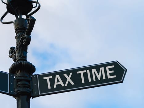 Street lighting pole with conceptual message TAX TIME on directional arrow over blue cloudy background.