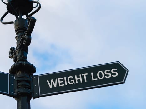 Street lighting pole with conceptual message WEIGHT LOSS on directional arrow over blue cloudy background.
