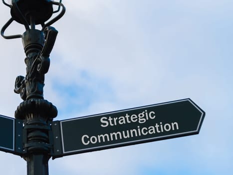 Street lighting pole with conceptual message Strategic Communication on directional arrow over blue cloudy background.