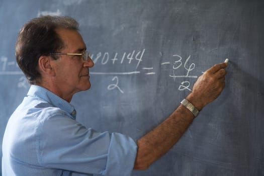 People and education. Teacher writing on math equation on blackboard during lesson.