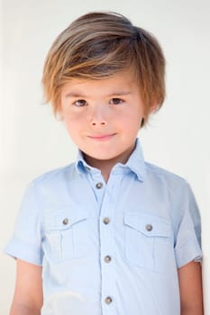 Portrait of a little boy against a white background. He is wearing a shirt and is smiling for the camera.