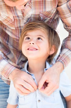 Close up of a little boy who is smiling at his father while he buttons up his shirt for him.