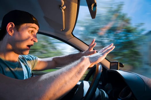 Side view of a young driver on the steering wheel blinded by the light of oncoming vehicles and with a shocked expression.