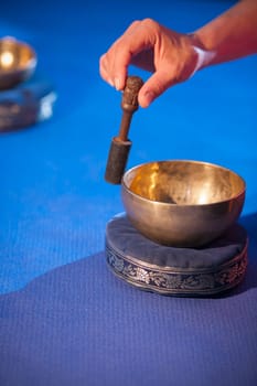 Close-up of a hand with bobbin lace and singing bowl on a blue background